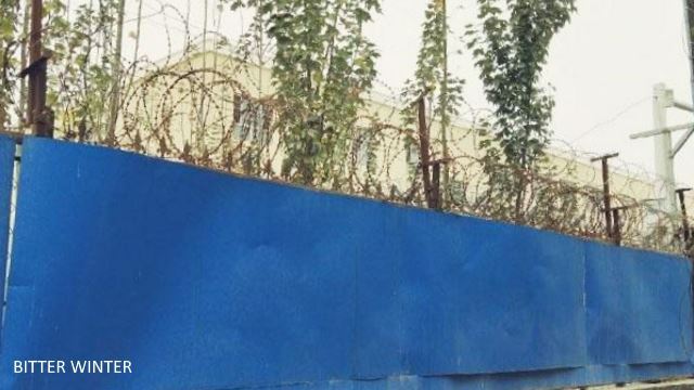 外圍牆是用藍色的彩鋼板圍成的，頂部裝置有螺旋型的鋼絲網