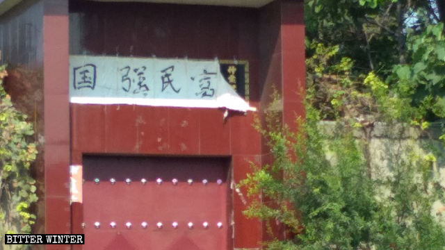 新安縣一戶人家門庭上的宗教牌匾被「國強民富」字樣遮蓋