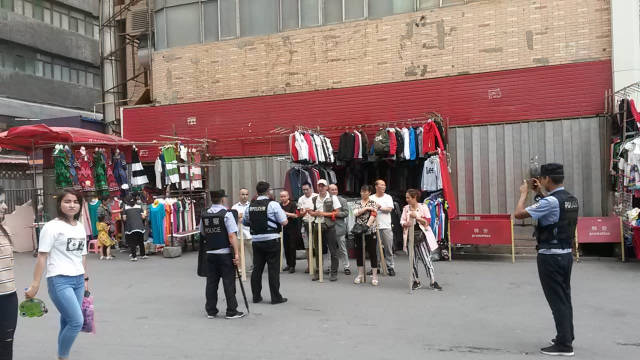 一場「持械」演習結束，烏魯木齊社區警察為後街商販拍照（2018年8月）