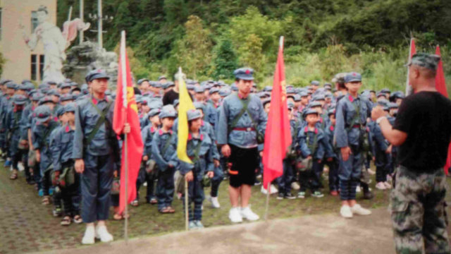 一群學生身穿紅軍服頭戴紅軍帽，背著印有毛主席頭像的包，上面寫著為人民服務。（微信圖片）