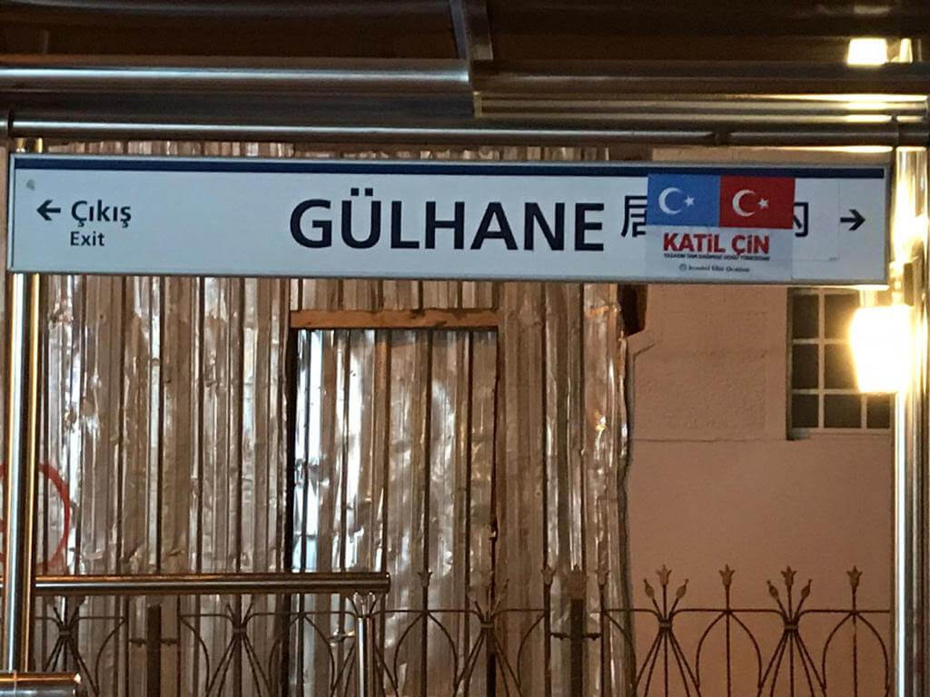 居尔哈内电车站的中文标牌被东突厥斯坦和土耳其的旗帜遮盖，上面写着「katil çin」（意思是「中国刽子手」）