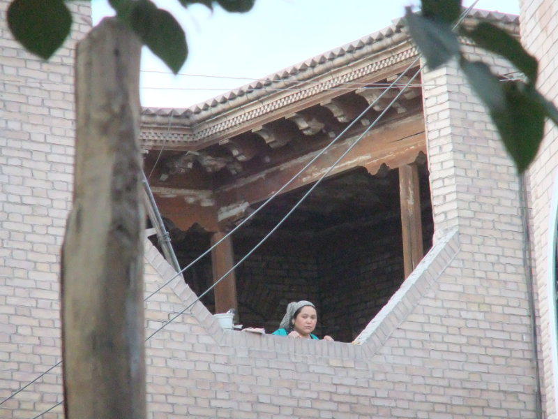 一婦人正從由水泥和磚改建後的家裡往外看。喀什　2012年